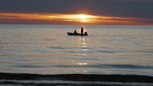 Fishermen in boat sail by sea at sunset