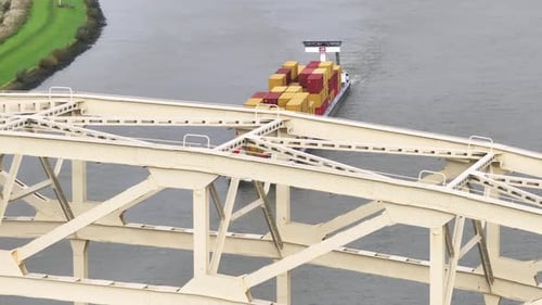 Aerial reveal of cargo vessel with goods sailing along wide river water