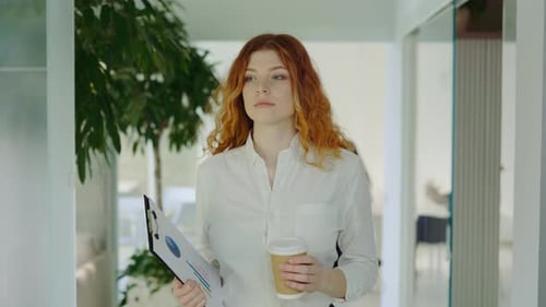 Businesswoman Walking with Coffee and Clipboard in Office