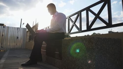 Successful Entrepreneur Works on Notebook Sitting on Bench at City Young Businessman Using Computer