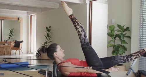 Fit senior caucasian woman stretching on reformer in pilates studio, unaltered, in slow motion
