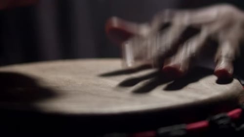 Nahaufnahme eines schwarzen Mannes, der eine afrikanische Volkstrommel spielt, dunkler Hintergrund im Studio