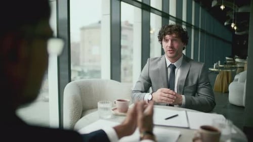 Businessman Smiling, Talking and Shaking Hands with Associate in Restaurant