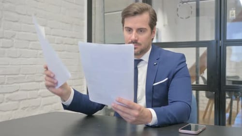 Man Reads Document and Celebrates Success at Desk