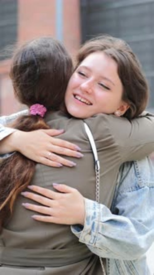 Vertical Young Woman Smiling Warmly While Hugging a Friend Outdoors in an Urban Area Expressing Joy