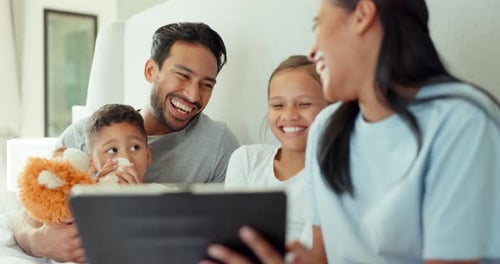 Family Laughing and Looking at Tablet in Bed