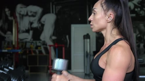A Brunette Works Out in the Gym She Lifts Dumbbells While Sitting in Front of a Mirror