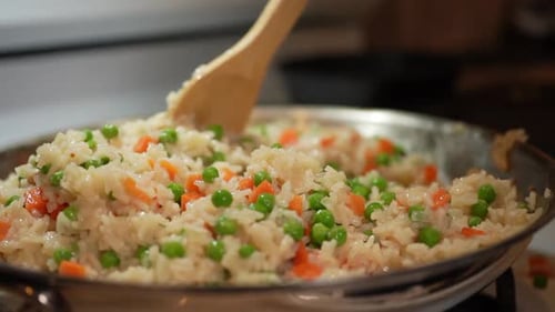 Stirring fried rice as it cooks on the wok with peas and carrots - slow motion