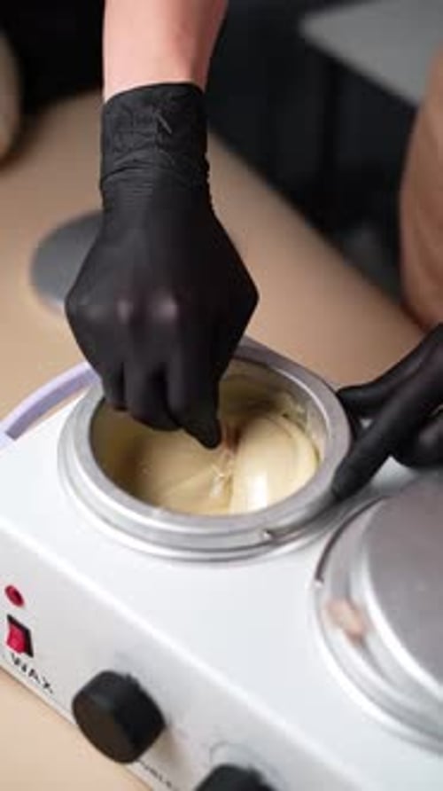 Master mixes the heating wax with a wooden spatula before the depilation procedure.