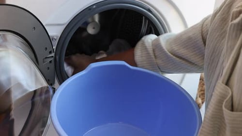 Woman taking laundry out of washing machine and putting into plastic basin indoors, closeup