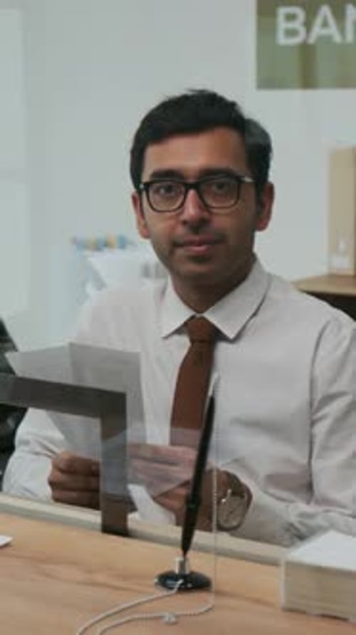 Portrait of Professional Indian Bank Teller Sitting Behind Service Window