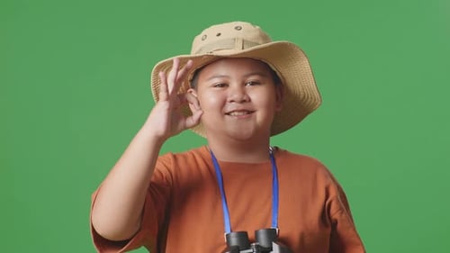 Asian Tourist Boy Researcher Using Binoculars, Showing Ok Gesture On Green Screen