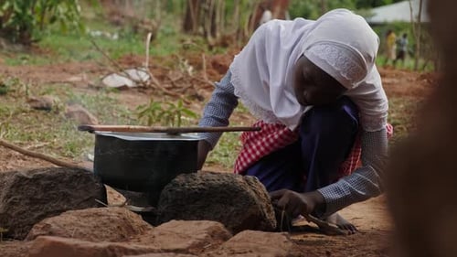 African Girl Cooking Over Fire with Firewood in Rural Village