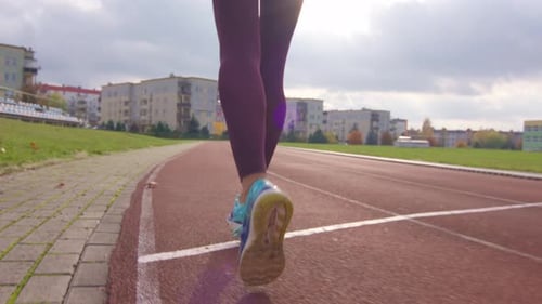 Low view of the legs of a young sporty girl running in slow motion on an athletic track while sunlig