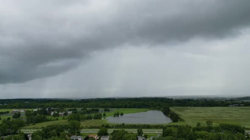 Drone footage of storm clouds rolling over green fields and a pond, capturing the dynamic weather pa