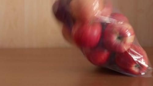 La mano de un hombre coloca una bolsa de plástico llena de manzanas rojas frescas sobre una mesa de madera y luego la recoge. Recicla