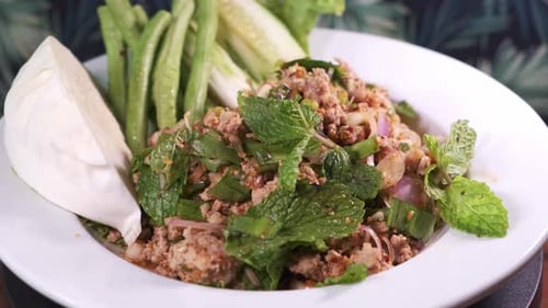 Authentischer thailändischer Larb Moo mit Minze und Gewürzen, frisch zubereitet, rotierend, auf einem weißen Teller, Nahaufnahme