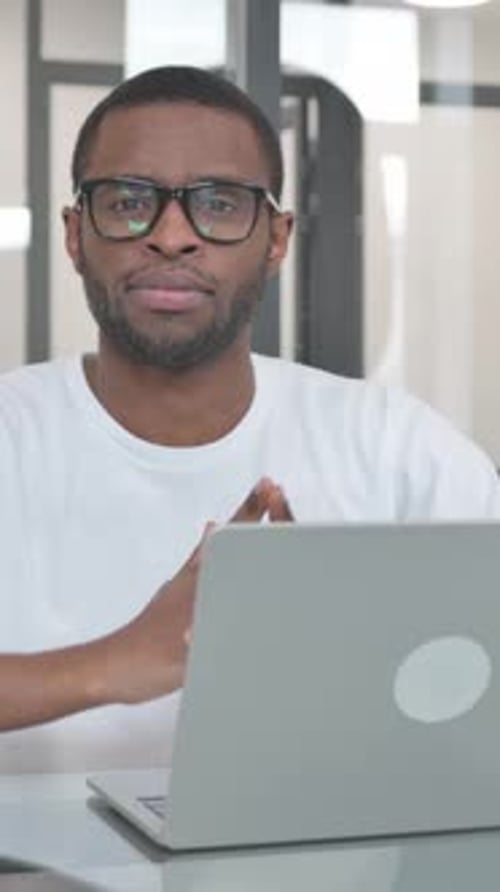 Young African Man Smiling at Camera while Working on Laptop in Office, vertical video