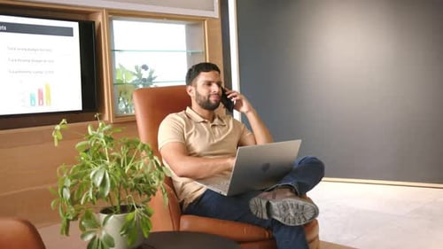 Working from home, man using laptop and talking on smartphone in office