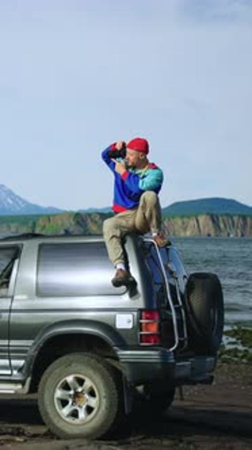 Man Sits on Car Taking Photos by Water