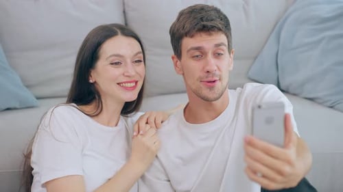 Caucasian attractive couple use mobile phone video call in living room.