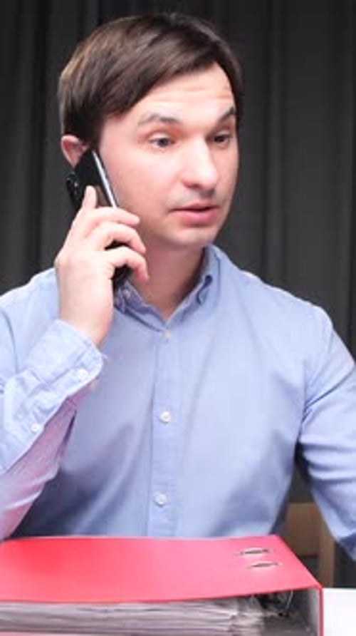 Vertical Video Office Worker Talking on Phone and Working on Laptop at Night