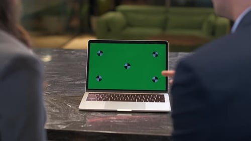 A man and a woman are discussing information on the green screen of a laptop.