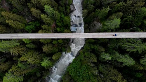 Top down aerial view of a hiker walking across a suspension bridge high up above Rhone river valley