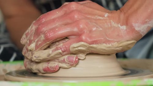 A female potter works on a potter's wheel, making a ceramic pot from clay in a pottery workshop.