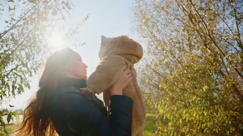Loving Mother Holding Baby in Sunny Grassy Field
