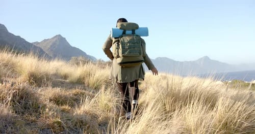 Woman Hikes Through Dry Grass toward Distant Mountains