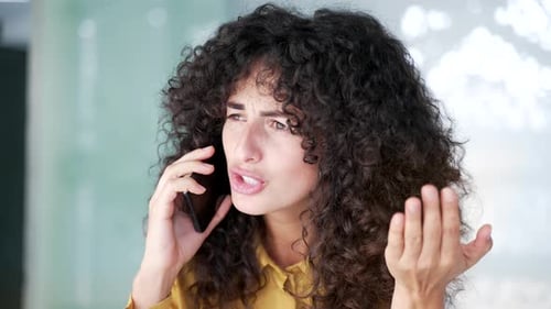 Angry female manager arguing talking on mobile phone at workplace in modern business office.