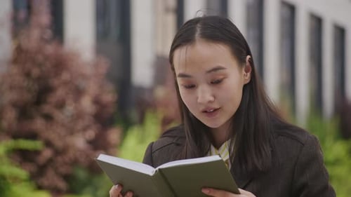 Woman Reading a Book Outdoors in Urban Setting