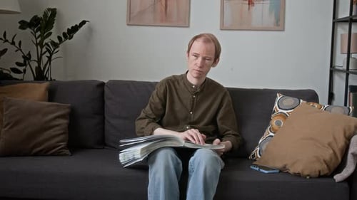 Young Adult Reading Book Sitting on Couch Indoors