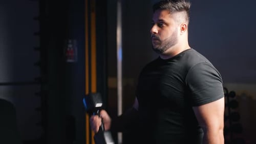 Junger starker Mann trainiert Bizepstraining mit Hantelgewicht im dunklen Fitnessstudio