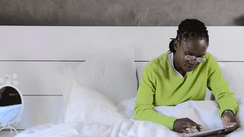 Man in bed smiles using tablet