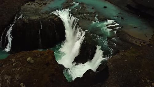 Aerial drone view above river water flowing down a large waterfall, in Iceland
