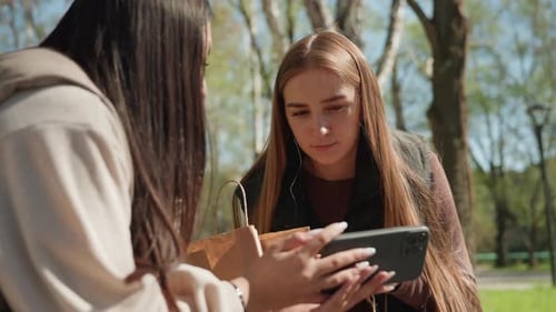 Caucasian Woman and Asian Friend Sharing Tablet in Park Focused Browsing and Discussion