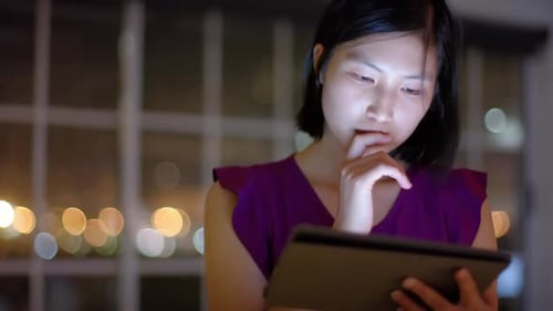 Thoughtful asian businesswoman using tablet by office window at night, slow motion