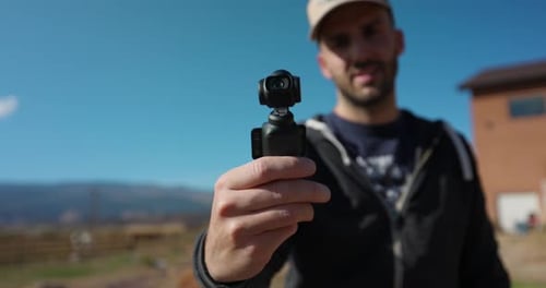 Male Freelancer Holding 3-Axis Stabilized 4K Handheld Camera And Moving Around With Hand. Bokeh Back
