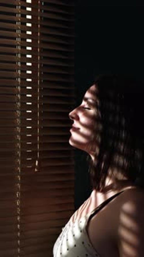 Belle jeune femme profitant de la lumière du soleil à travers les stores à la maison