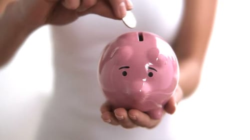 Unrecognizable woman holds piggy bank up against white studio backdrop