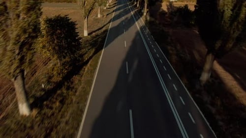 Revealing drone shot of a paved road leading towards mountains, on a clear sunny day