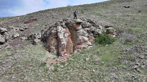 Figure Stands Triumphant on Rocky Hillside