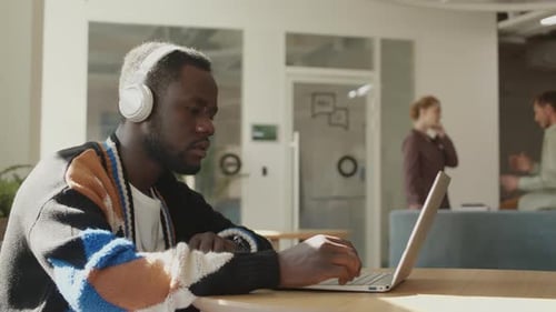 African American Man in Headphones Using Laptop in Office