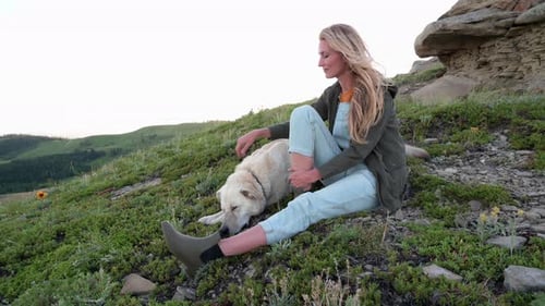 Woman Petting Dog While Sitting on Grassy Hill