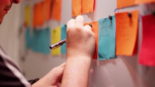 Man Writing on Sticky Note in Creative Workspace Close-Up