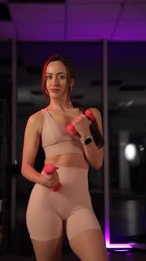 A Fit Young Woman Performs Strength Training with Dumbbells in a Stylish Night Gym Vertical Video
