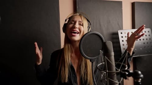 girl singer singing in a recording studio with headphones in front of microphone to create a song