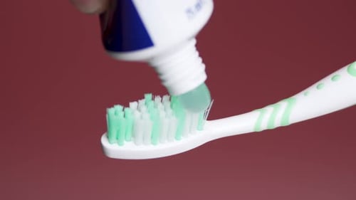 Toothpaste is applied to a toothbrush from a tube.